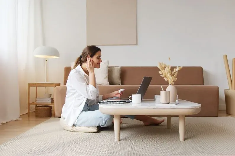 Une femme assise dans un salon calme échange en visio sur son ordinateur portable.